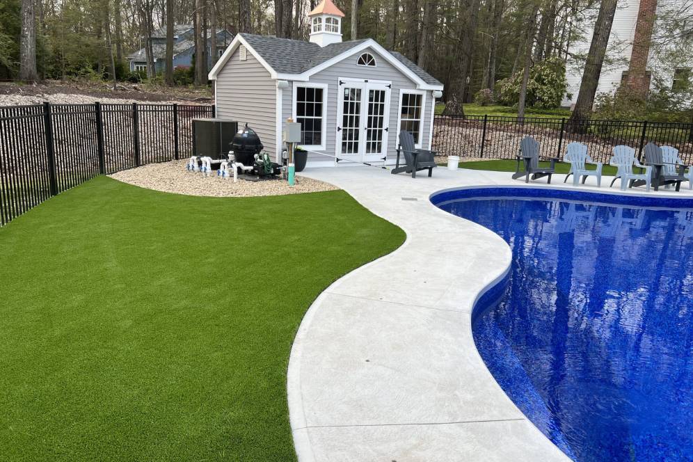 Backyard with a synthetic lawn, poolside chairs, a shed, and a curved blue swimming pool